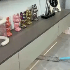 Orvenisa limpiando el hueco de debajo de un mueble de salón, a ras de suelo