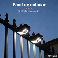 Foco solar sujeto con pinza a una valla de noche
